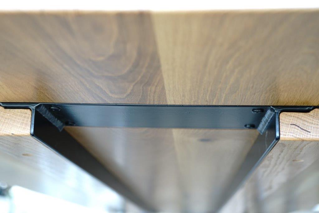 Close-up view of a wooden table underside showing a black steel table base supporting the structure, part of an **American White Oak Dining Table** from our collection of handcrafted dining room furniture by **Timber Grooves**.