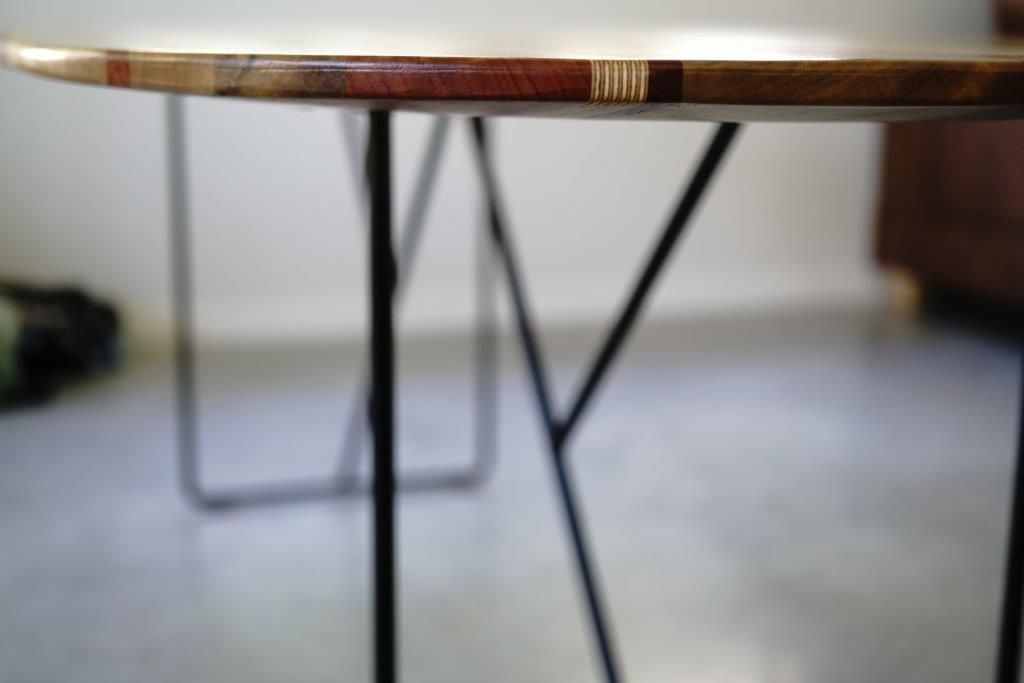 Close-up of a handcrafted table with metal legs on a polished concrete floor. The focus is on the edge of the Timber Grooves Surfboard Dining Table, highlighting its smooth finish, unique grain patterns, and exceptional craftsmanship.