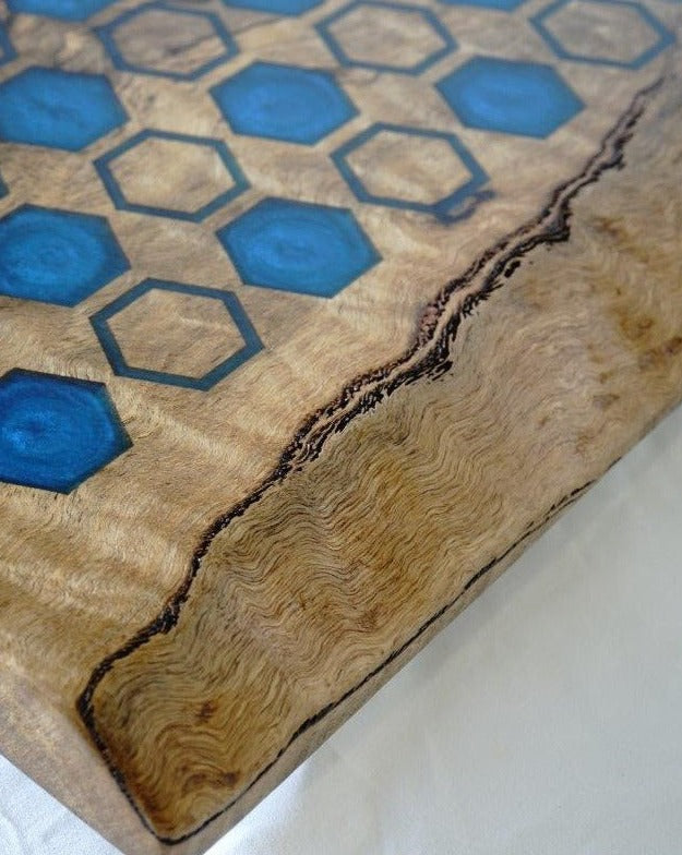 Close-up of a Timber Grooves Chessboard with Resin Inlay surface featuring blue hexagonal resin inlays and a live edge on one side. The Australian hardwood has a natural grain pattern.