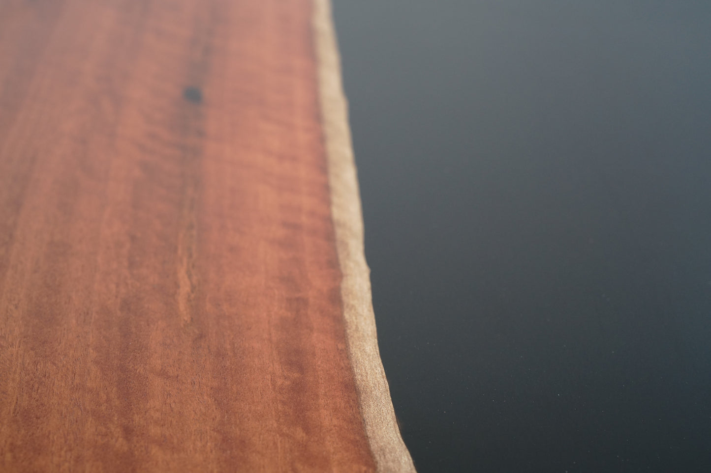 Close-up of a Timber Grooves Jarrah Tuxedo Coffee Table showing a smooth transition from polished wood on the left to a black resin surface on the right, accented by elegant marri bowties.