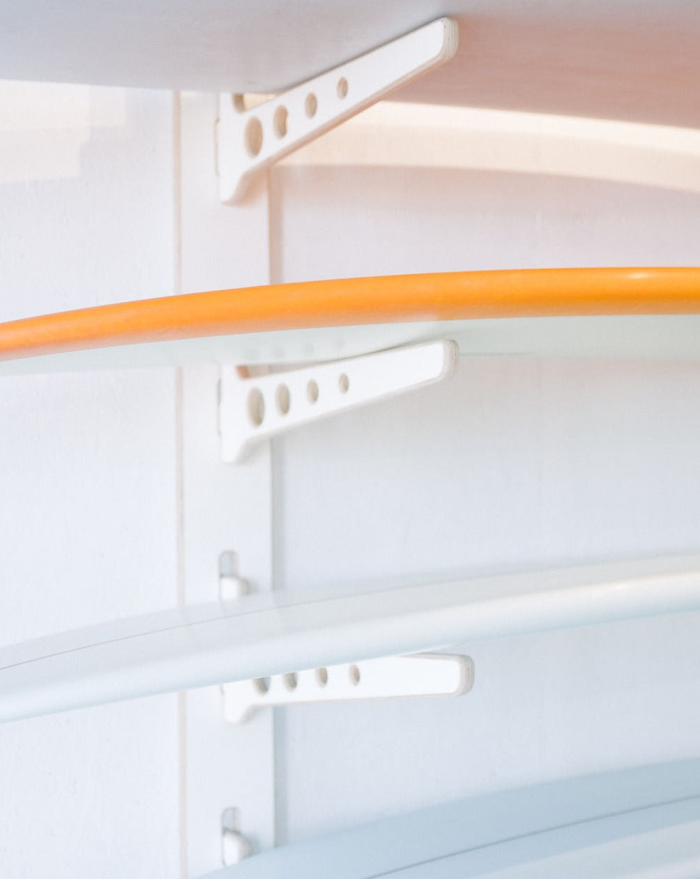 A stylish Timber Grooves Surfboard Rack Wall Mount holds multiple surfboards against a pristine white wall.