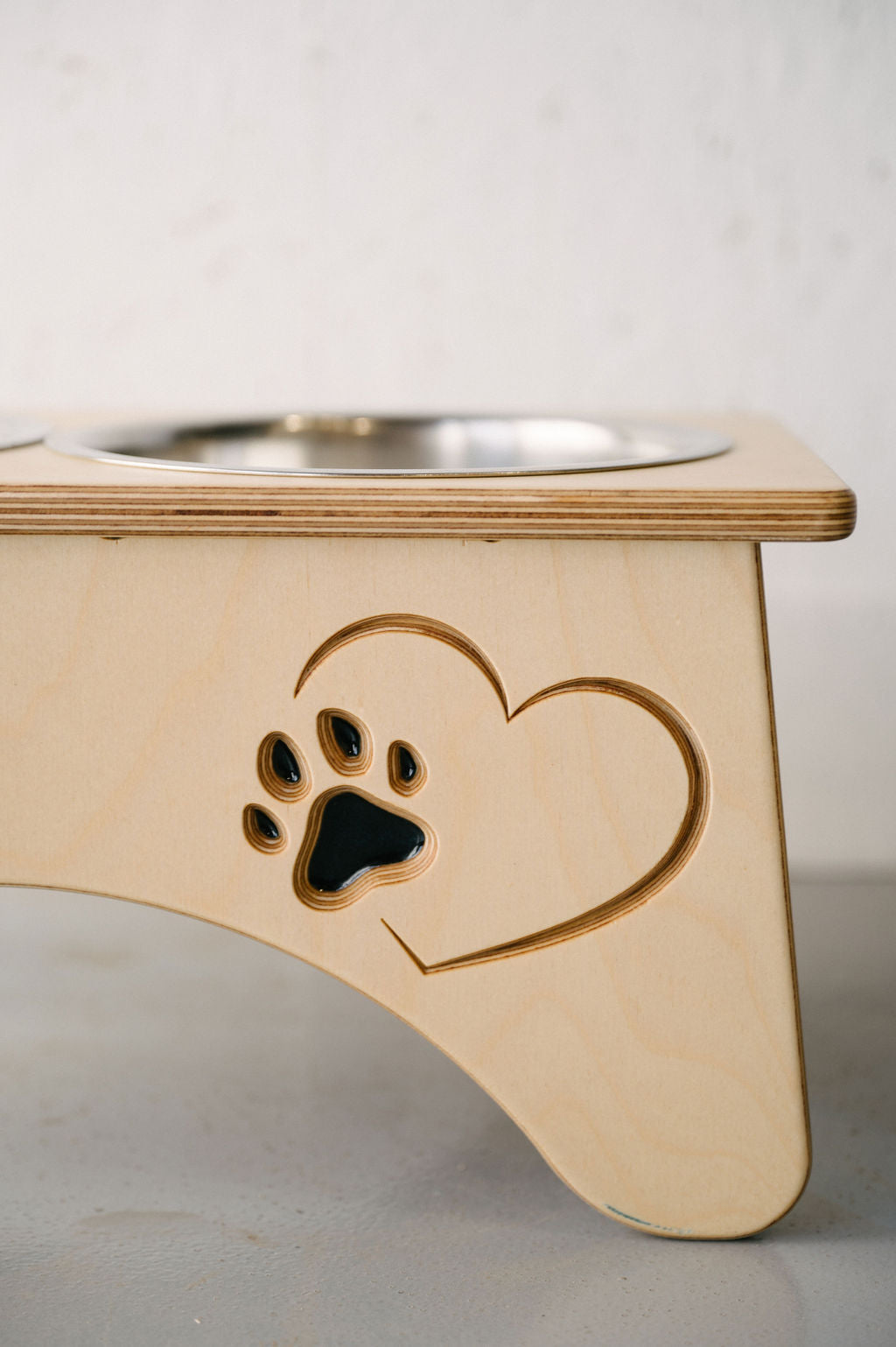 A Timber Grooves Double Raised Dog Bowl Stand with a heart and paw print design, holding stainless steel bowls, helps reduce symptoms of bloat and alleviate skeletal and joint pain for your furry friend.