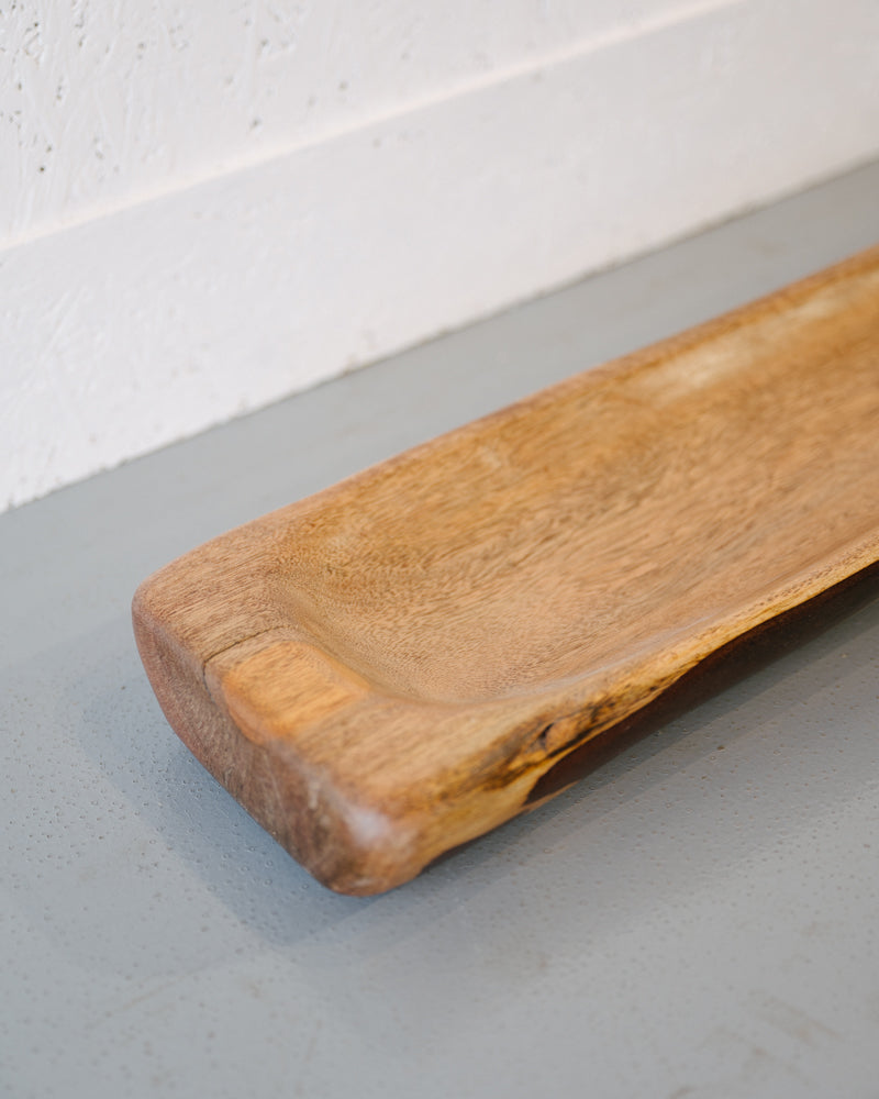 A close-up of the Timber Grooves Centre Piece Bowl with a light brown finish, showcasing its natural wood grain, placed on a gray surface near a white textured wall.