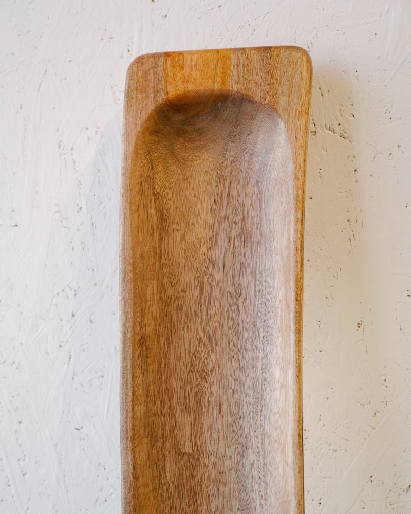 A close-up of the Centre Piece Bowl by Timber Grooves, a rectangular wooden tray with a shallow indent, showcasing the natural wood grain, seen against a textured white wall background.