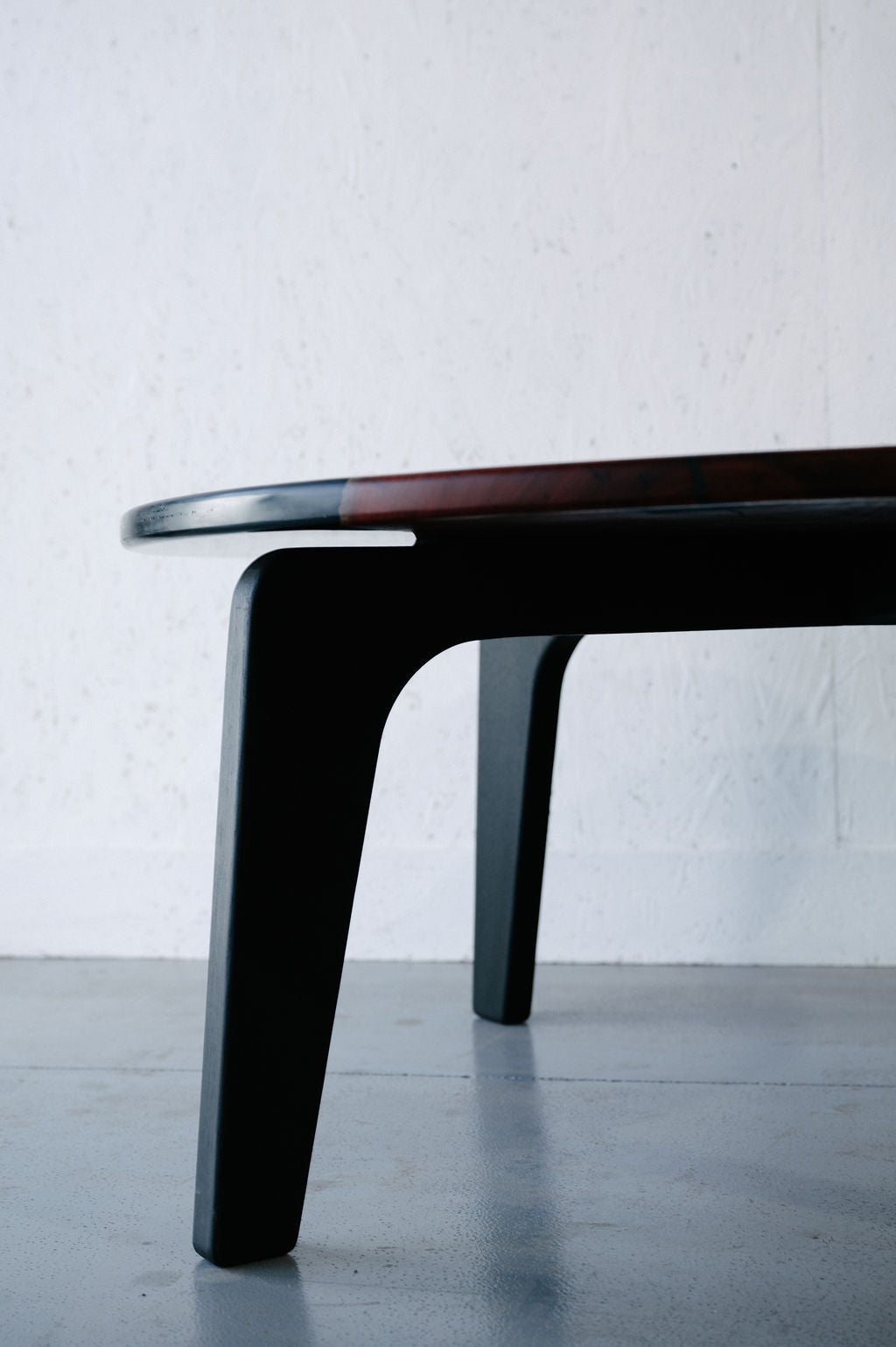 Close-up view of the legs and edge of a Timber Grooves Jarrah Tuxedo Coffee Table set against a white wall and gray floor.