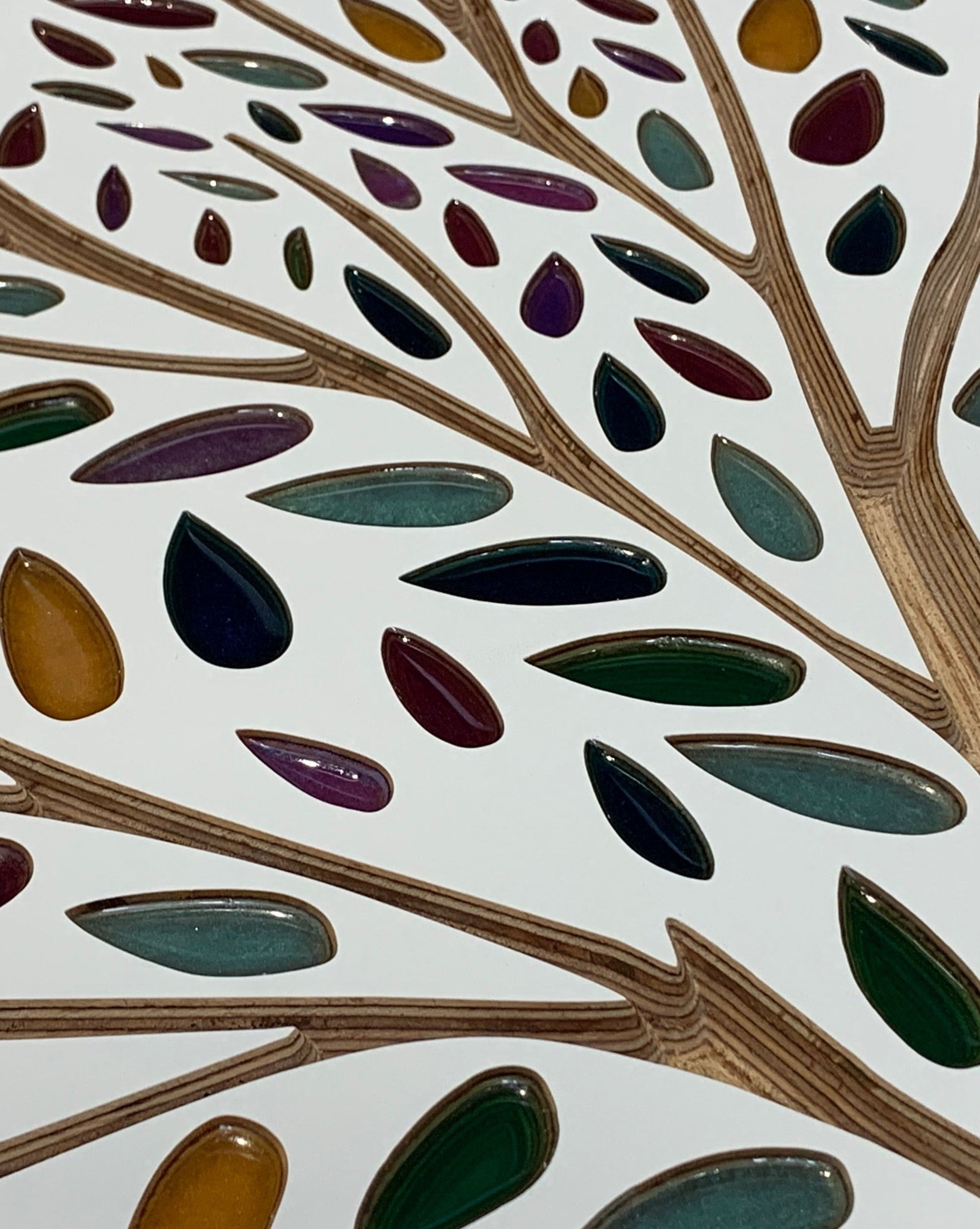 Close-up of an artistic Resin leaves Tree of Life in White by Timber Grooves made with variously colored, teardrop-shaped resin filled leaves embedded in a white background.