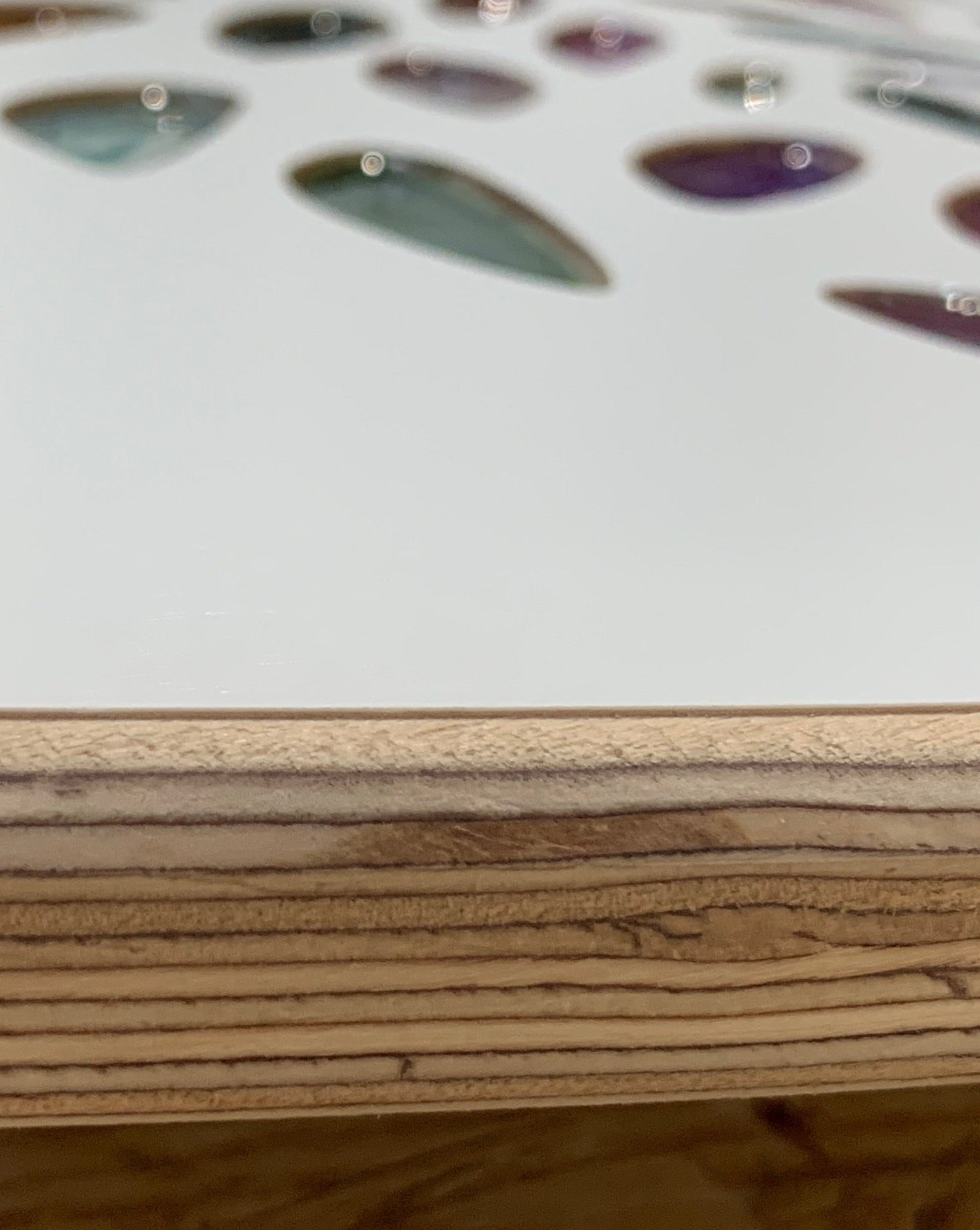 A close-up of colorful, teardrop-shaped inlays embedded in a light wooden surface, resembling Resin leaves Tree of Life in White by Timber Grooves, with part of the edge showing visible wood grain.