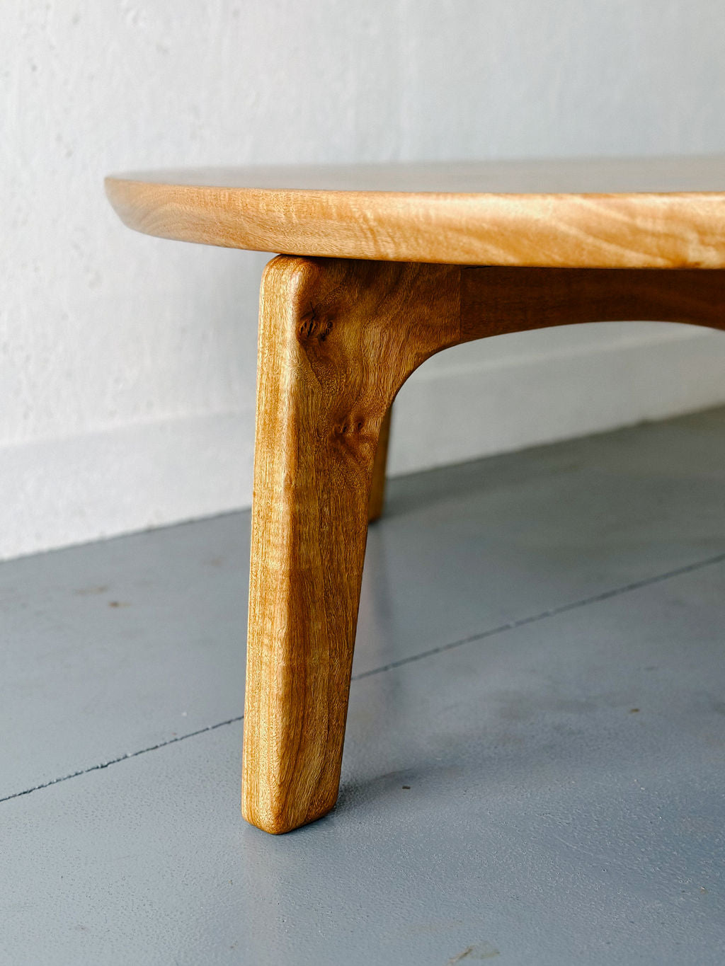 Close-up of a handcrafted Marri Coffee Table leg with a smooth finish by Timber Grooves, made from Australian Hardwood, set against a simple white wall and gray floor background.