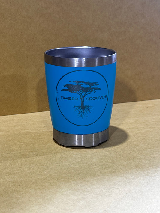 A stylish and sustainable option, the Laser Engraved Keep Cup by Timber Grooves features a blue, eco-friendly design with a silver rim and base, showcased against a beige background. The cup is personalized with a laser-engraved logo of a tree alongside the brand name, "Timber Grooves.