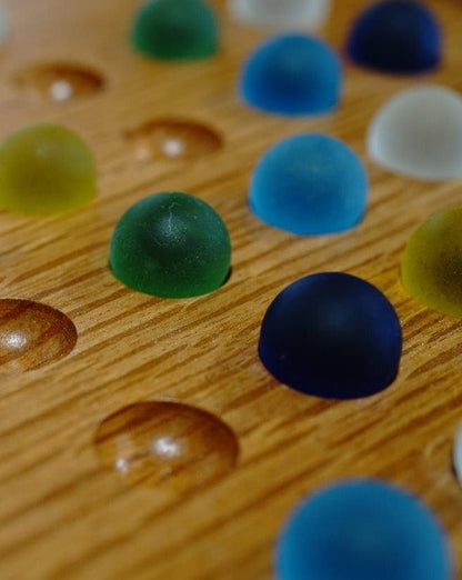 Colorful, translucent hemispherical pieces on a wooden board, forming Timber Grooves' Solitaire game with matching concave recesses.