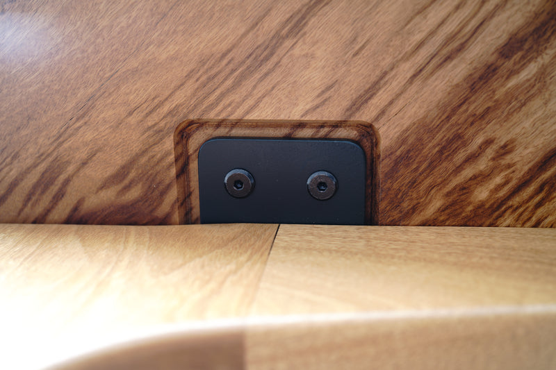Close-up of a Timber Grooves Marri Dining Table surface with a small rectangular dark plate featuring two screws. The wood grain and the fitted components are prominently visible, showcasing the table's handcrafted elegance.