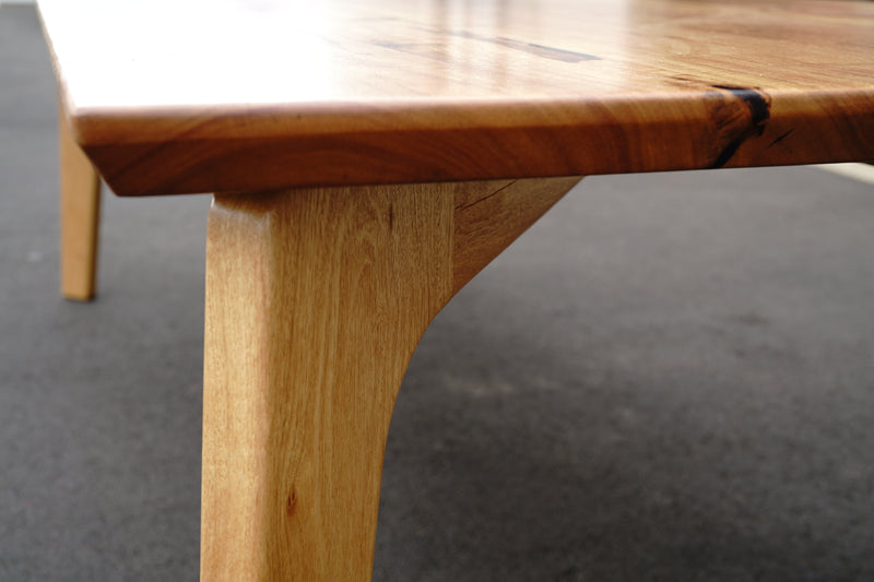 Close-up of the corner of a handcrafted wooden table with a smooth finish and visible natural grain, set against a dark background, exuding the elegance of a Marri Dining Table by Timber Grooves.