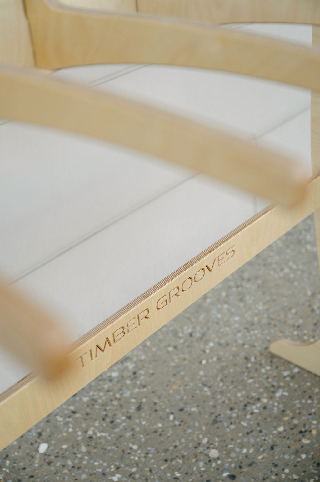 Close-up of a Surfboard Rack Freestanding with the words "Timber Grooves" engraved on the underside. The surfboard rack is on a speckled floor, reminiscent of the craftsmanship seen in custom surf racks.