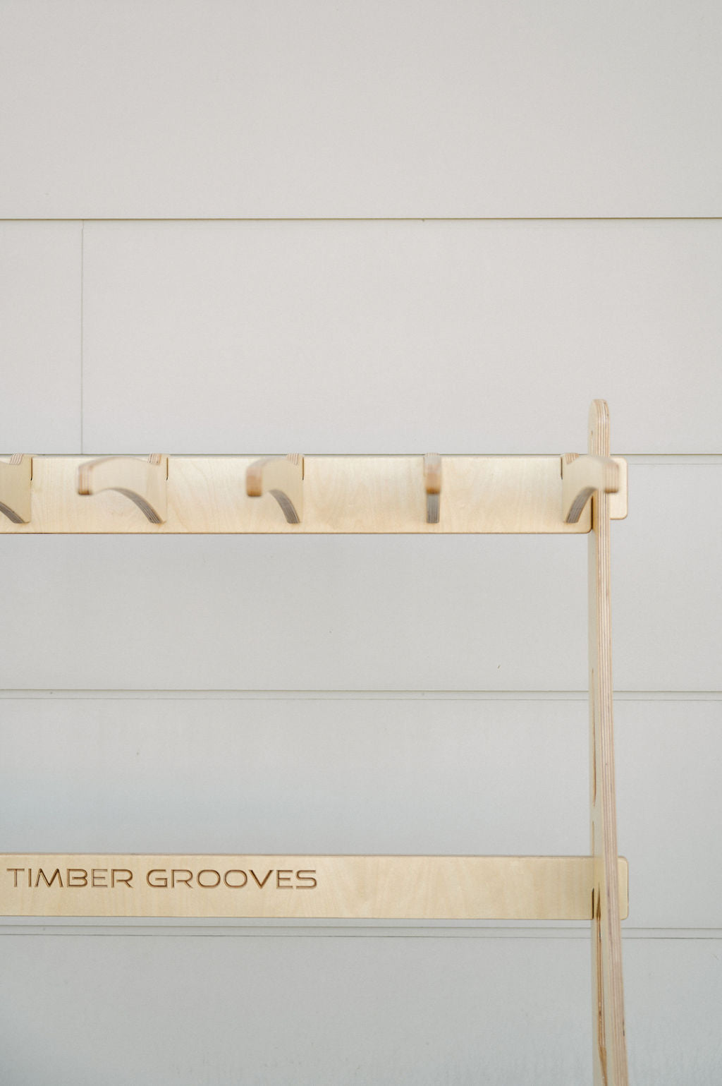 A wooden rack labeled "Timber Grooves," mounted on a light-colored wall, features multiple evenly spaced hooks for hanging items. Ideal for various uses, this Timber Grooves Surfboard Rack Freestanding also caters to wholesale inquiries for businesses needing quality wall-mounted racks.