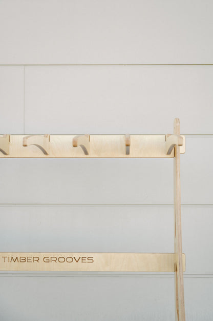 A wooden rack labeled "Timber Grooves," mounted on a light-colored wall, features multiple evenly spaced hooks for hanging items. Ideal for various uses, this Timber Grooves Surfboard Rack Freestanding also caters to wholesale inquiries for businesses needing quality wall-mounted racks.