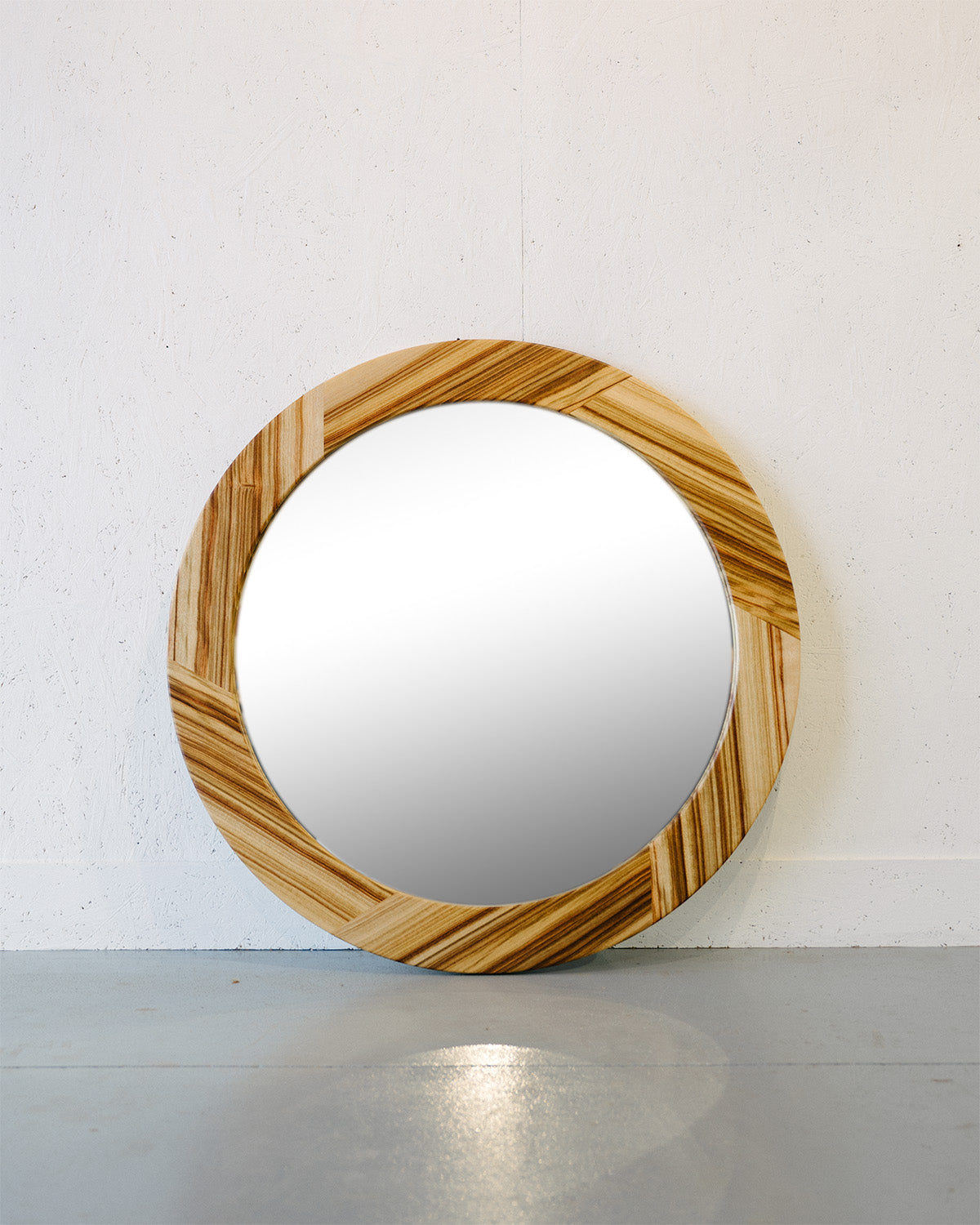 Timber Grooves' Camphor Laurel Mirror with a shatter-proof design and a wooden frame featuring alternating light and dark wood patterns, leaning against a light-colored wall on a gray floor.