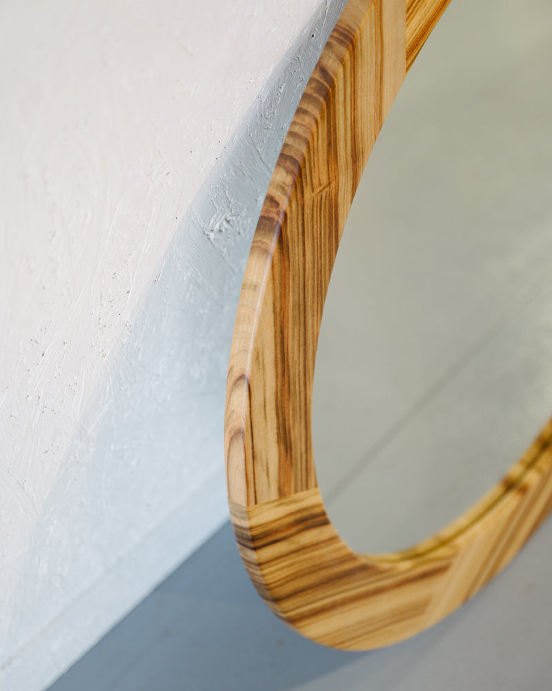 Close-up of Timber Grooves' unique Camphor Laurel Mirror with a smooth, polished surface against a textured white background.