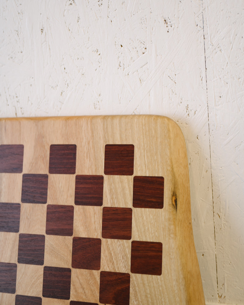 Close-up of a Timber Grooves Marri Chessboard with Jarrah Inlay with alternating light and dark squares set against a textured white background wall, perfect for premium chess games.