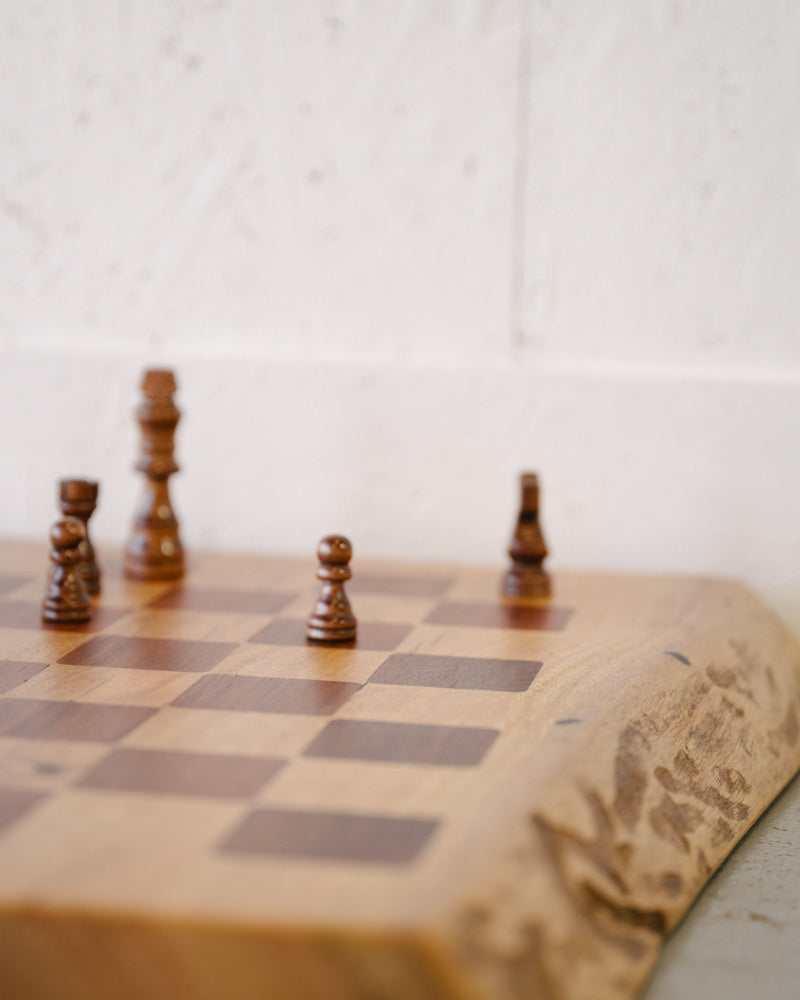 Wooden chess pieces are positioned on a Timber Grooves Marri Chessboard with Jarrah Inlay, showcasing the elegance of chess games against a light background.