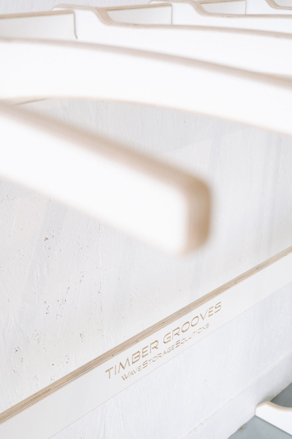 Close-up of white coat hangers on a wall-mounted rack with the inscription "Surfboard Rack Freestanding by Timber Grooves." Custom surf rack and wholesale inquiries welcome.