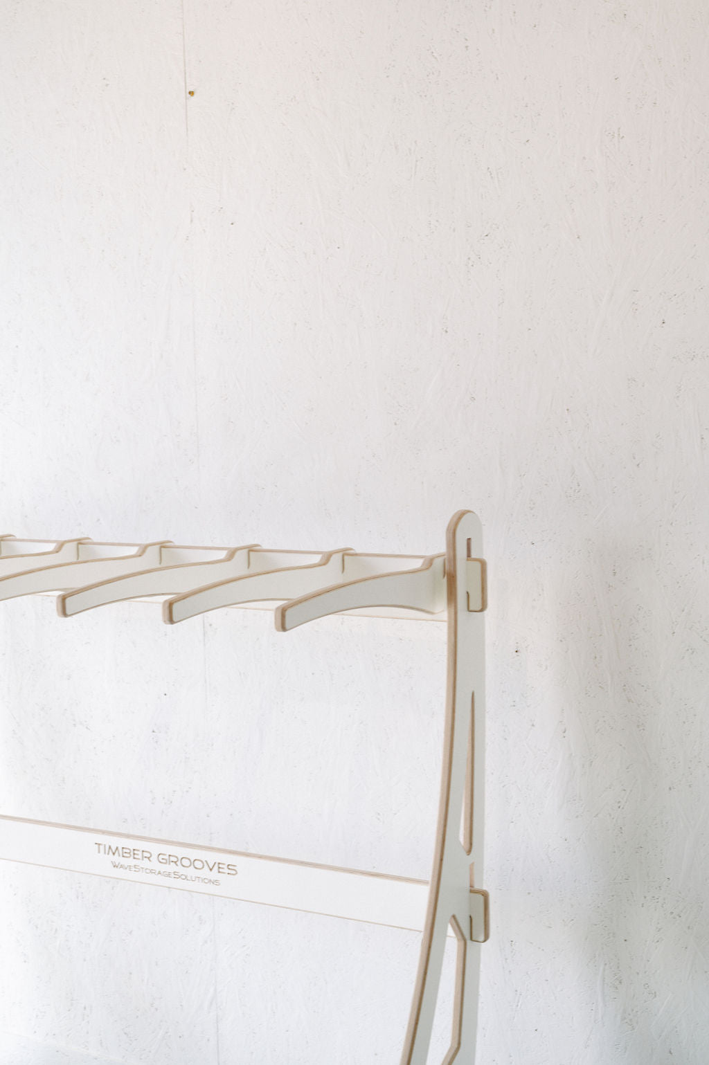 The Surfboard Rack Freestanding by Timber Grooves, featuring multiple hooks, stands elegantly against a textured white wall.