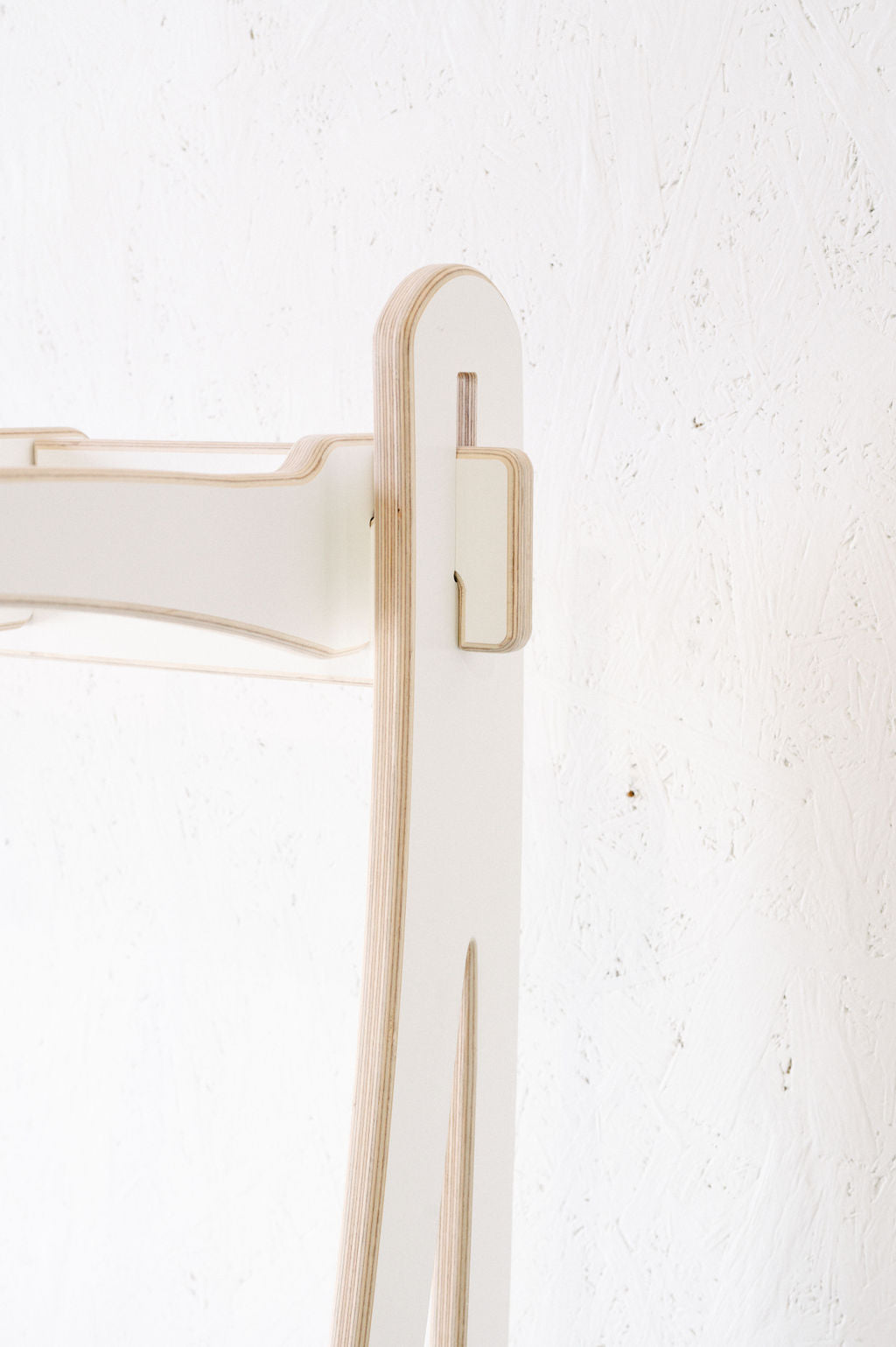 Close-up view of a white wooden structure with a minimalist design, resembling the Surfboard Rack Freestanding by Timber Grooves, set against a textured white wall.