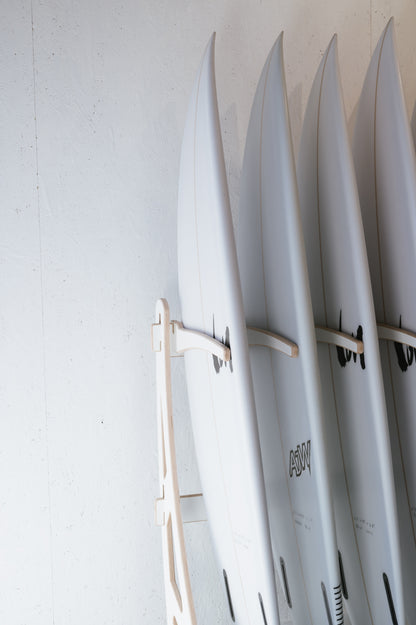 Four white surfboards are neatly arranged upright on a wooden rack against a white wall. Wholesale inquiries for our custom Surfboard Rack Freestanding by Timber Grooves can help you organize your gear like a pro, ensuring everything is stylishly displayed and easily accessible.