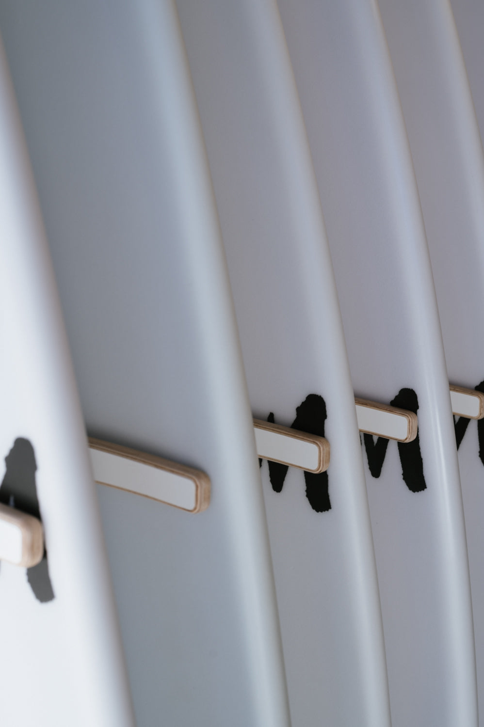 Close-up image of white surfboards lined up with wooden stringers and black markings along their sides, elegantly displayed on the Surfboard Rack Freestanding by Timber Grooves.