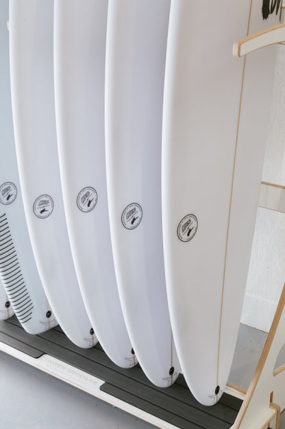 A row of five white surfboards neatly arranged on a Timber Grooves Surfboard Rack Freestanding against a white wall. For wholesale inquiries about our stylish and functional wall-mounted racks, please contact us directly.