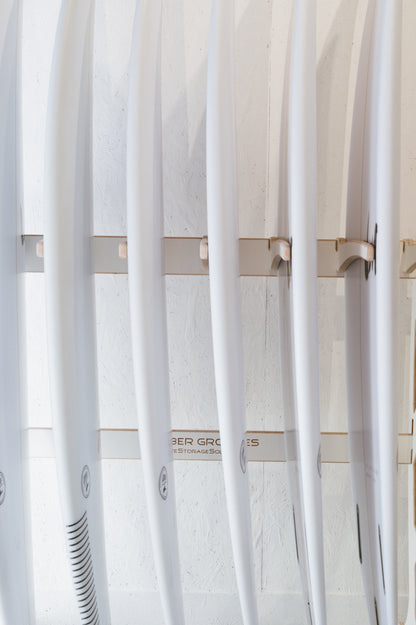 A row of white surfboards vertically lined up in a Surfboard Rack Freestanding by Timber Grooves against a white wall.