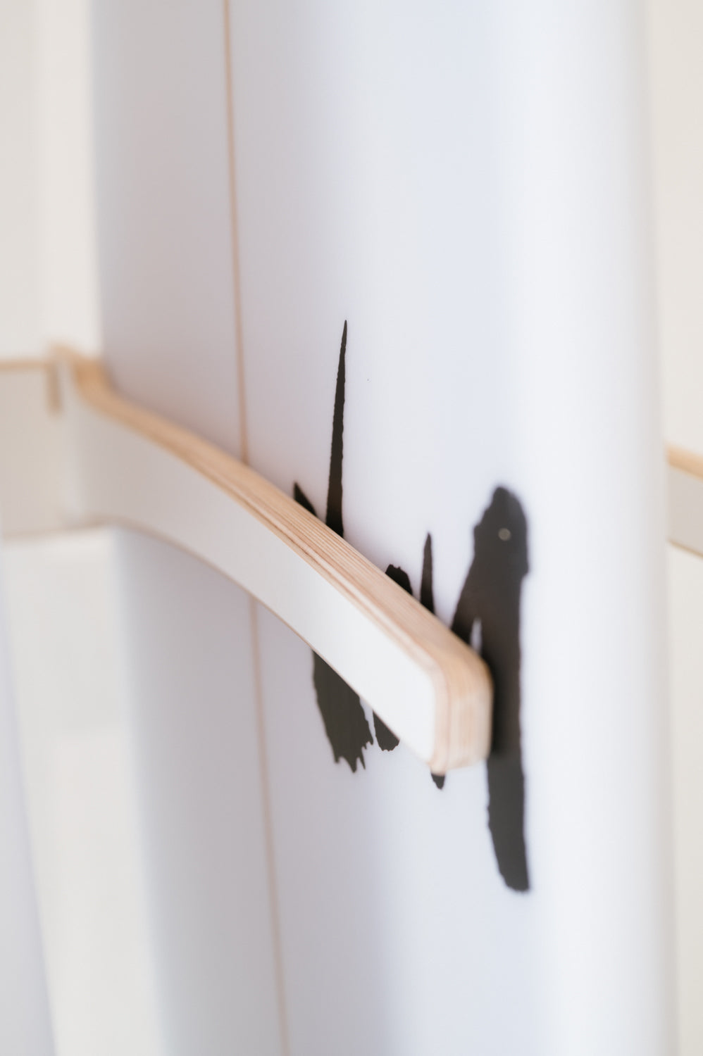 Close-up of a Surfboard Rack Freestanding by Timber Grooves with black abstract design and a wooden or beige handle attached horizontally, perfect for those interested in custom surf rack designs. Wholesale inquiries are welcome for these unique wall-mounted racks.