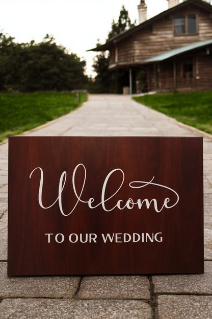 A Personalised Timber Wedding Welcome Sign by Timber Grooves adorns a stone pathway leading to a rustic house nestled in greenery, adding a touch of rustic elegance.