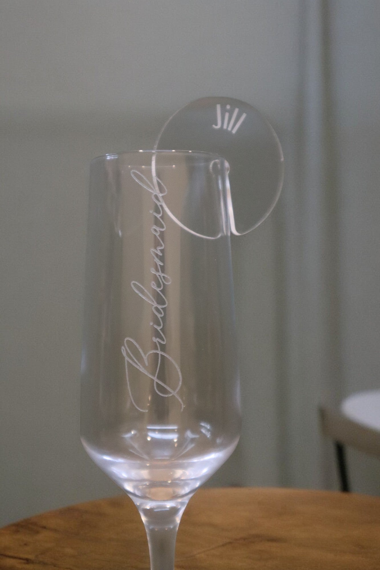 A clear wine glass labeled "Bridesmaid" showcases a Timber Grooves Personalised Acrylic Drink Tag elegantly engraved with the name "Jill," making it ideal for an elegant table setting.