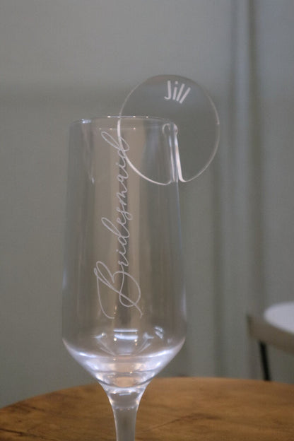 A clear wine glass labeled "Bridesmaid" showcases a Timber Grooves Personalised Acrylic Drink Tag elegantly engraved with the name "Jill," making it ideal for an elegant table setting.