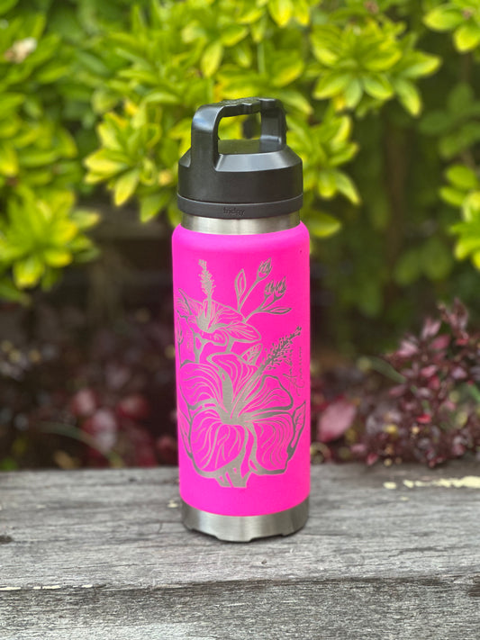 A Custom Laser Printed Water Bottle by Timber Grooves, featuring a vibrant pink hue and long-lasting stainless steel construction with floral designs, rests on a wooden surface amidst verdant greenery.